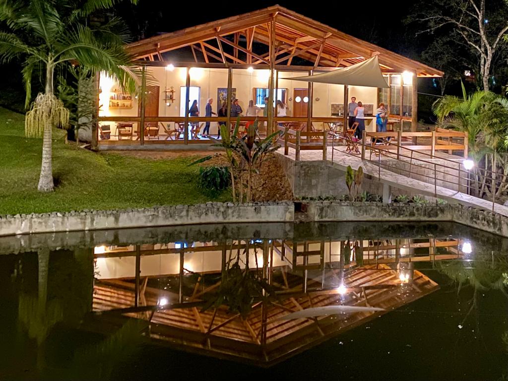 Salão iluminado do Espaço Dois Leões refletido na água à noite